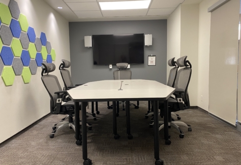 A table, six chairs, a monitor on the wall, and a wall ornament inside the Gallery Room at New Westminster Public Library's Main Branch.