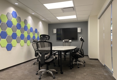 A table, six chairs, a monitor on the wall, and a wall ornament inside the Gallery Room at New Westminster Public Library's Main Branch.