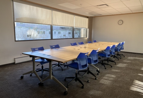 A table, 12 chairs, a clock on the wall, and a large window inside the Ash Street Room at New Westminster Public Library's Main Branch.