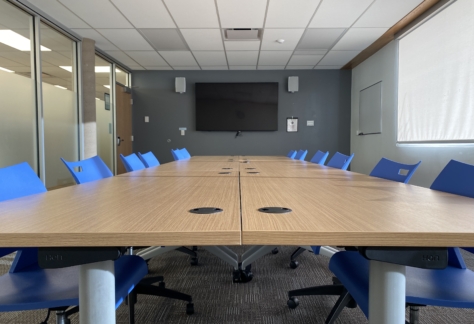 A table, 12 chairs, and a monitor on the wall inside the Ash Street Room at New Westminster Public Library's Main Branch.