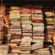 Stacks of old paperback books are lit with a beautiful yellow light from a window.