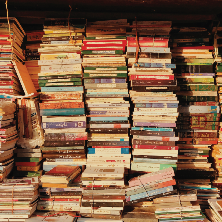 Stacks of old paperback books are lit with a beautiful yellow light from a window.