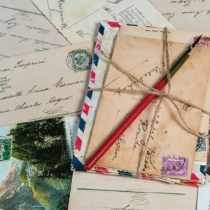 A pile of postcards are loosely tied with a string. On top of the bundle is an old-fashioned fountain pen.