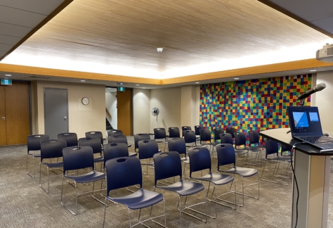 Chairs in rows, a lecturn, laptop, and microphone inside the Auditorium at New Westminster Public Library's Main Branch.
