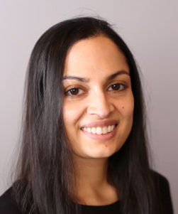 Against a grey backdrop, a south Asian woman with long dark hair smiles into the camera.