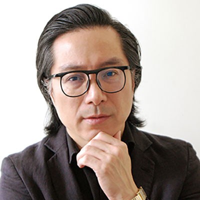 Against a white background, an Asian man with glasses looks toward the camera with his hand at his chin.