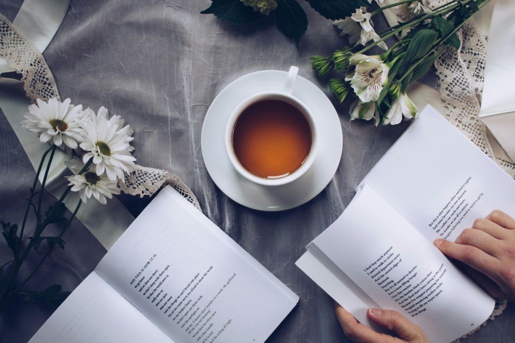 Two open poetry books, a cup of tea, and white flowers on a table.