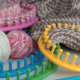 colourful round, plastic knitting looms, some empty, some looped with yarn, sit on a table with some balls of yarn.