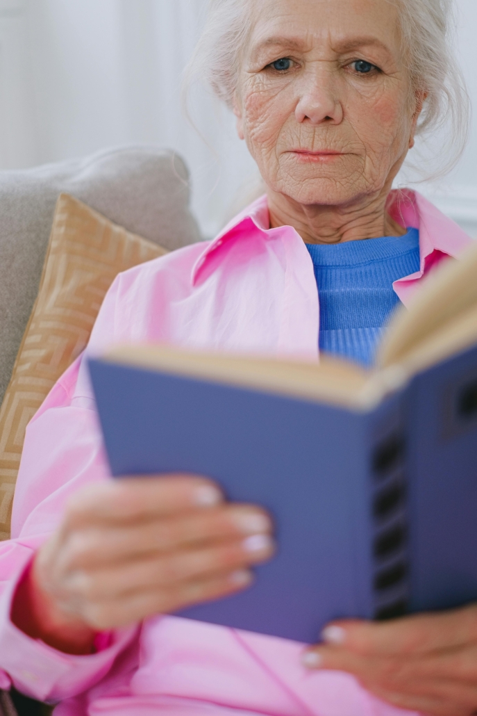 An older adult in a pink shirt reads a book with a purple cover.