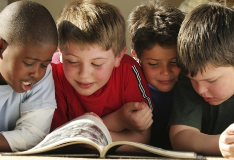 Close-up of four boys reading a book on the ground.
