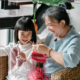 A young girl and a grandmother are knitting together and have big smiles.