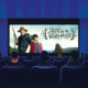 In a darkened movie theatre, an audience sees the promo image for the film Hunt for the Wilderpeople on a screen.