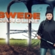 A fierce looking woman with a pitchfork and wearing a toque stands in front of giant fork tines.