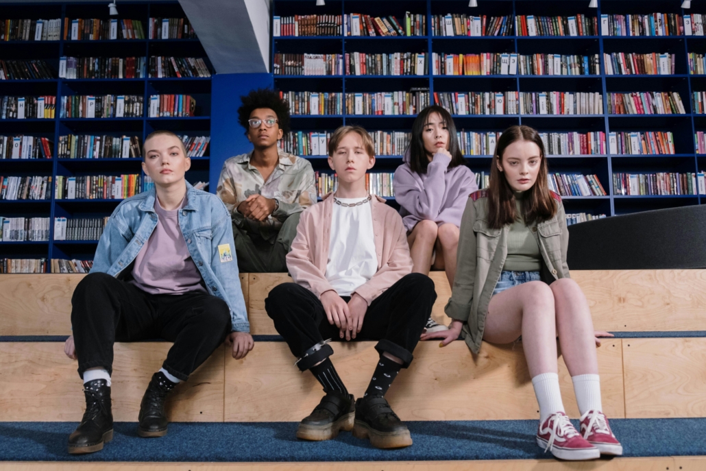 Five teens sit on steps with bookshelves behind them.