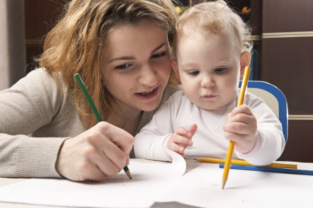 Adult and toddler use pencils to draw.