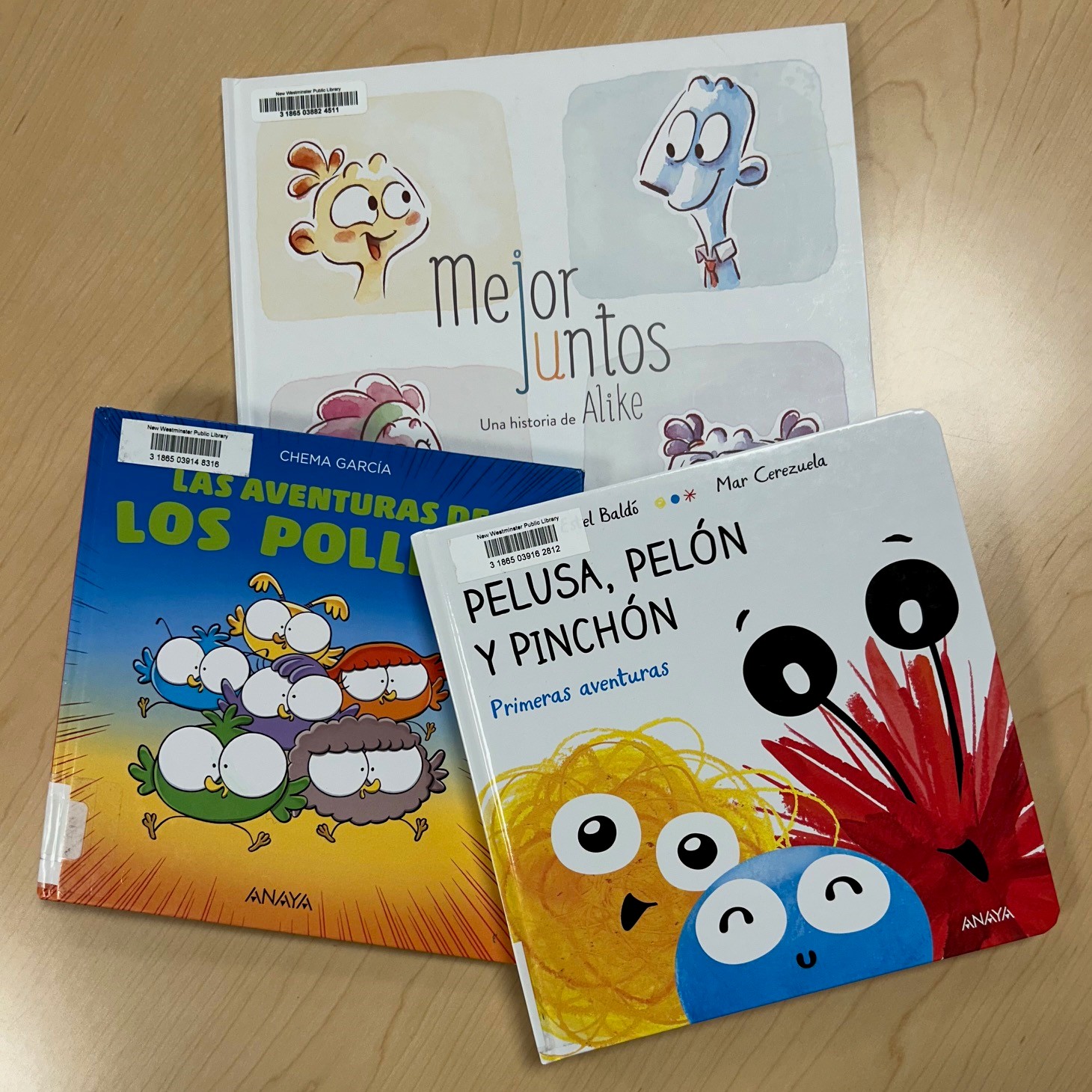 Three Spanish-language picture books on a wooden table.