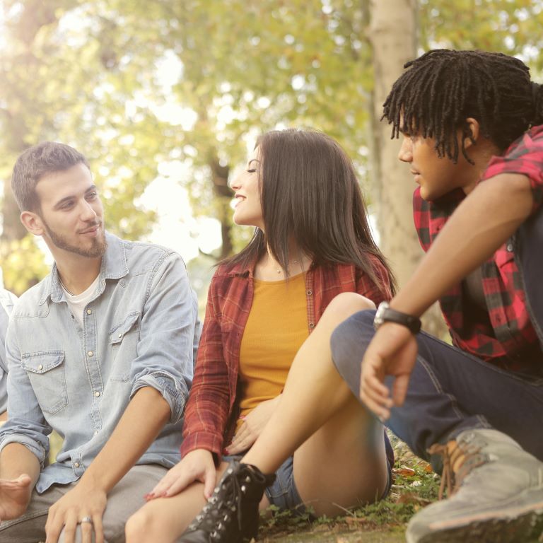 Three young adults chat outside in a treed area.