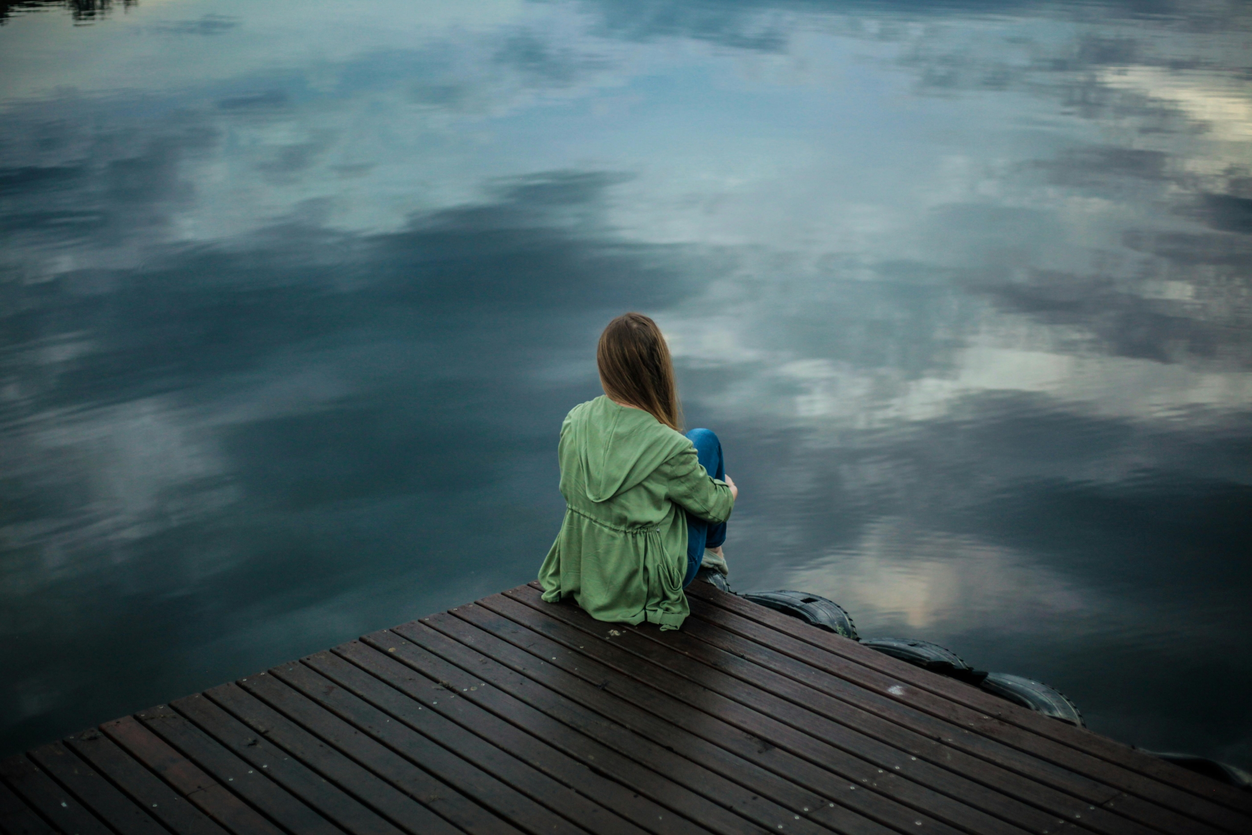 A person sits on the edge of the dock looking out at the water. Their face is unseen.